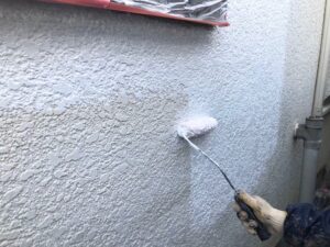 外壁に白いペンキをローラーで塗装