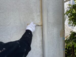 調布市　外壁塗装　ハケで薄いグレーに塗られる堅樋の裏の外壁