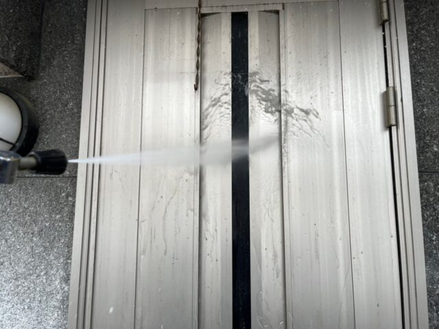 高圧洗浄機で洗浄される調布市の住宅の銀色のドア