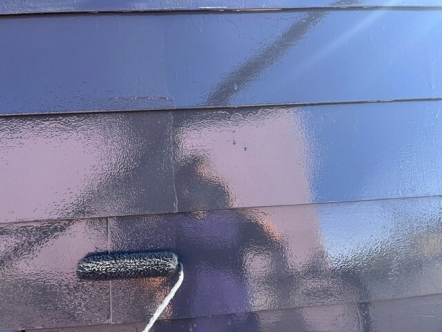 ローラーで黒に塗装される調布市の住宅の屋根