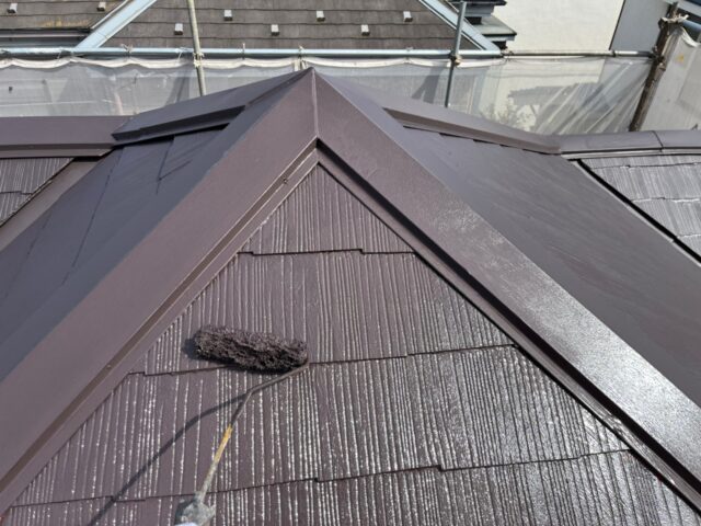 ローラーで茶色に塗られる三鷹市の住宅の屋根